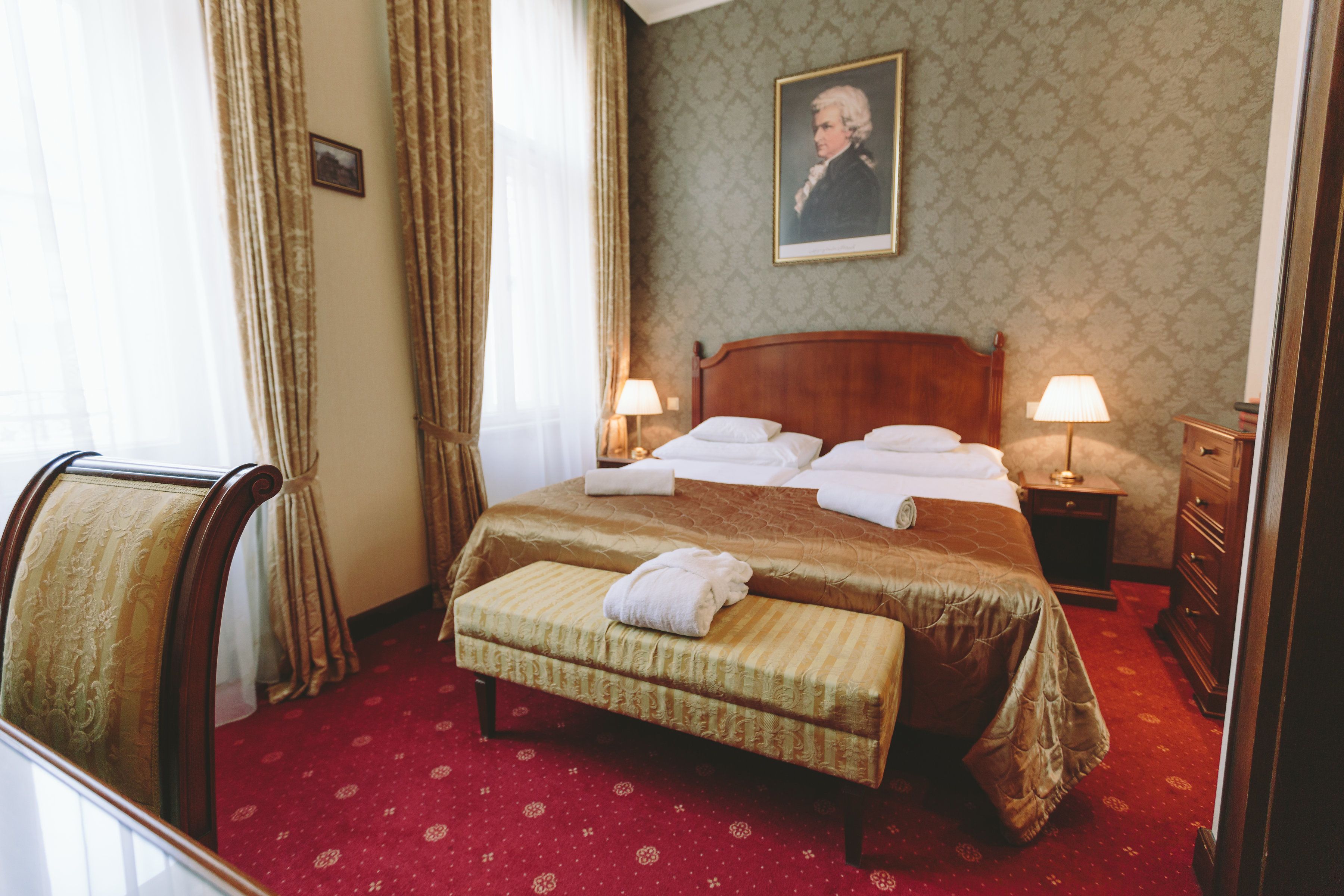 A hotel room with a large bed, a bench, a nightstand, and a dresser.