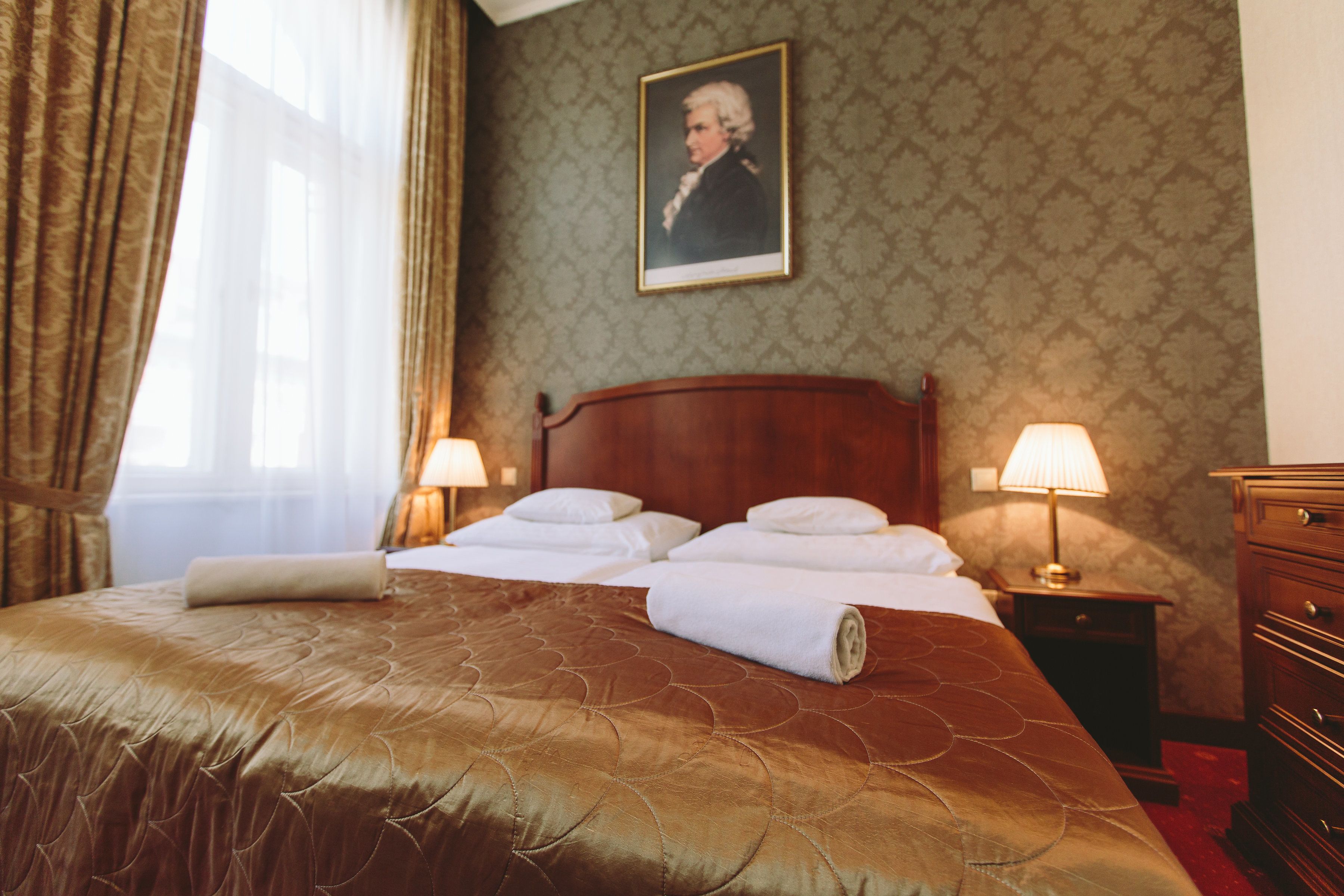 A hotel room with a large bed, two bedside lamps, a wooden nightstand, and a portrait on the wall.
