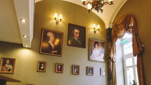 A lobby with a chandelier, framed portraits, and a checkered floor. - Mozart Hotel (Szeged)