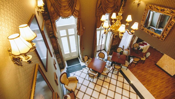 A hotel lobby with a checkered floor, a dining area with a table and chairs, and a chandelier. - Mozart Hotel (Szeged)