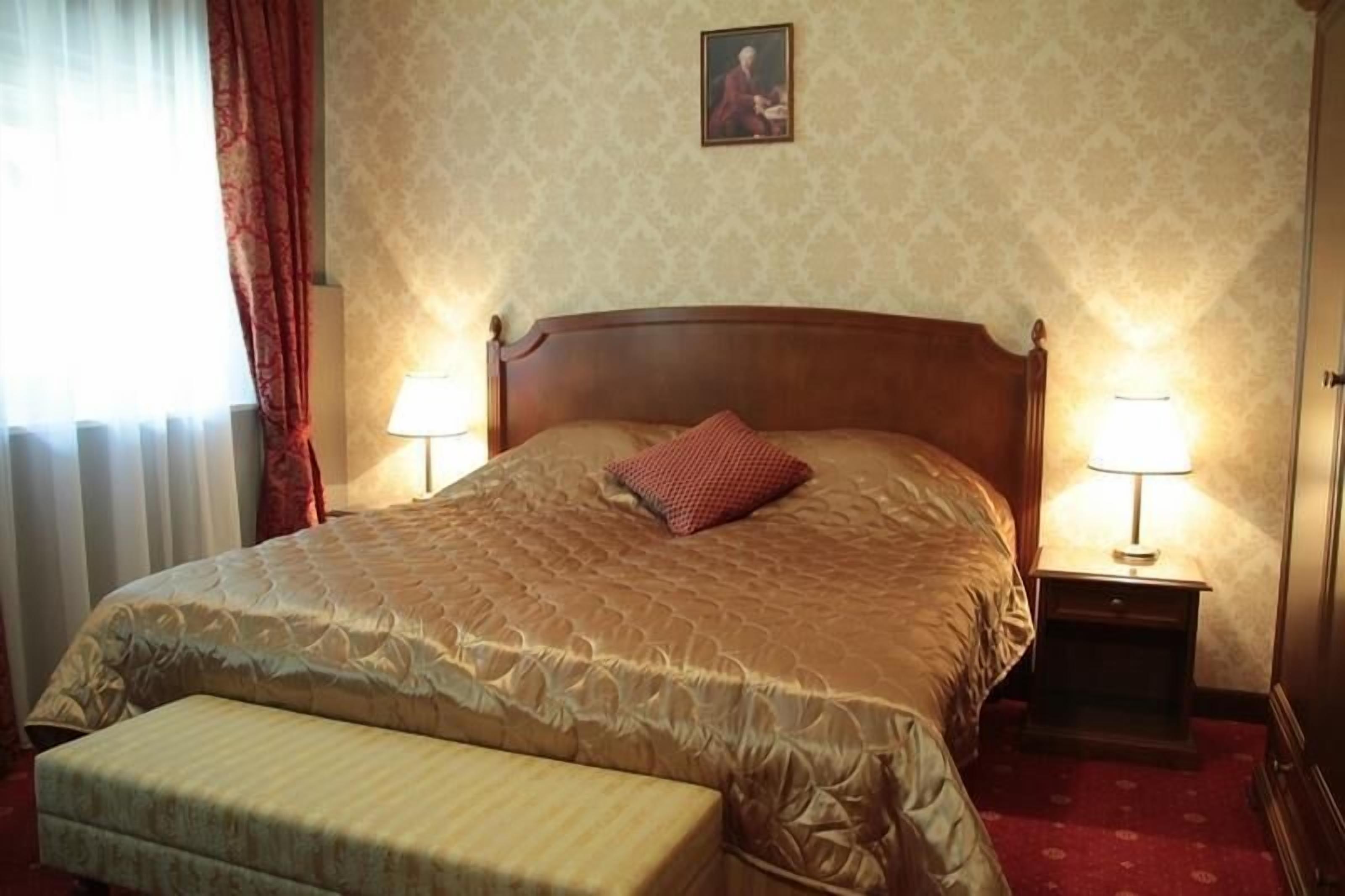 A neatly made bed with a quilted headboard, a single pillow, and a bedside table with a lamp.