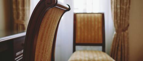 Una silla de madera con asiento y respaldo acolchados, ubicada en una habitación con ventana y cortinas.
