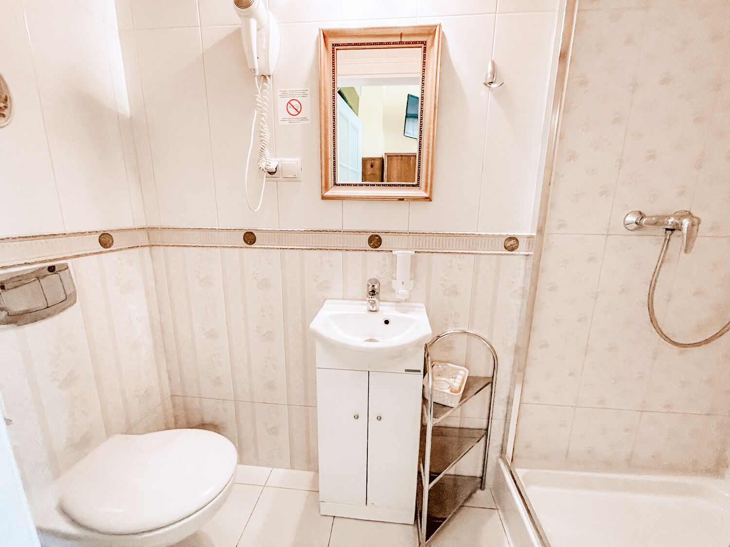 A small bathroom with a toilet, sink, and shower. There is a hairdryer on the wall, a mirror above the sink, and a towel rack.
