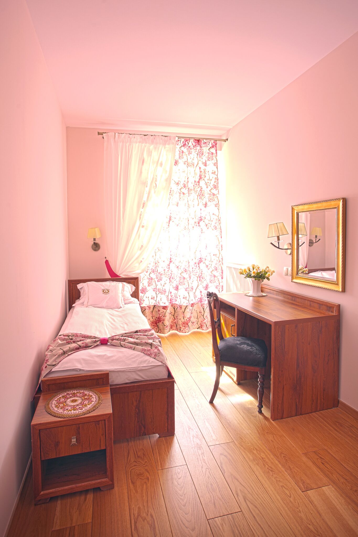 Une chambre à coucher comprenant un lit, un bureau, une chaise, une table de chevet et une fenêtre avec des rideaux.