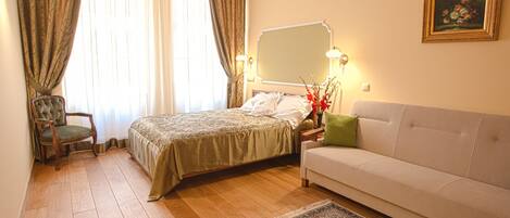 A hotel room with a bed, a sofa, a chair, a large mirror, and a painting on the wall.