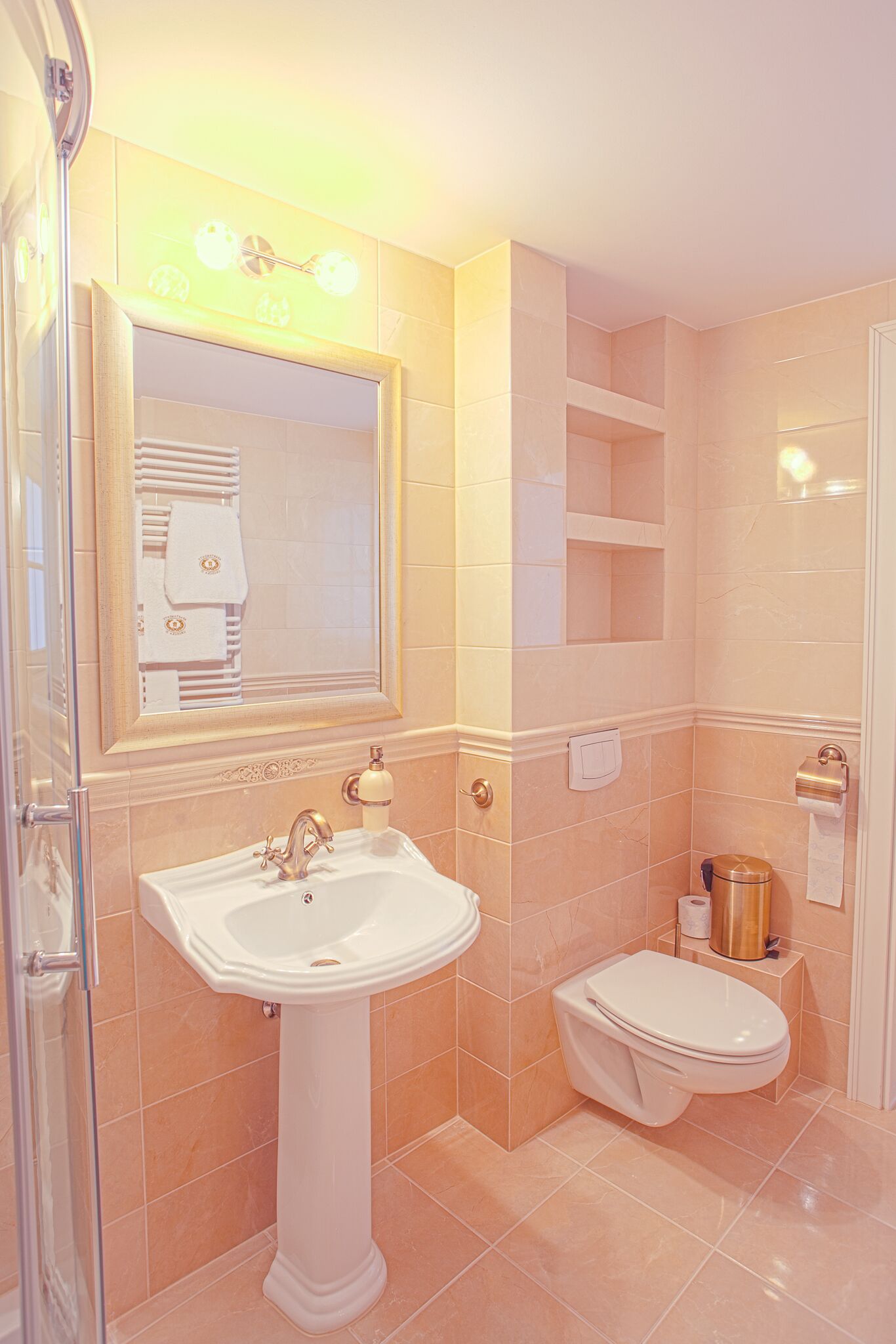A bathroom with a pedestal sink, a toilet, a mirror, and a shower area.