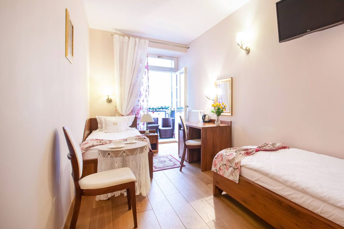 Een hotelkamer met een bed, een bureau, een stoel, een klein tafeltje en een raam met gordijnen.