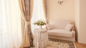A cozy living room with a white sofa, a lace-covered table with a vase of flowers, and a patterned rug. - Aparthotel Grodzka 21 (Kraków)