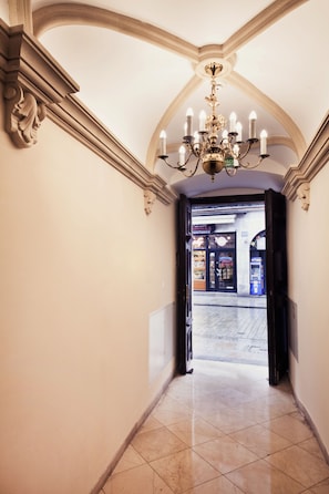 A hallway with a chandelier, a door leading to a public area, and a tiled floor. - Aparthotel Grodzka 21 (Kraków)