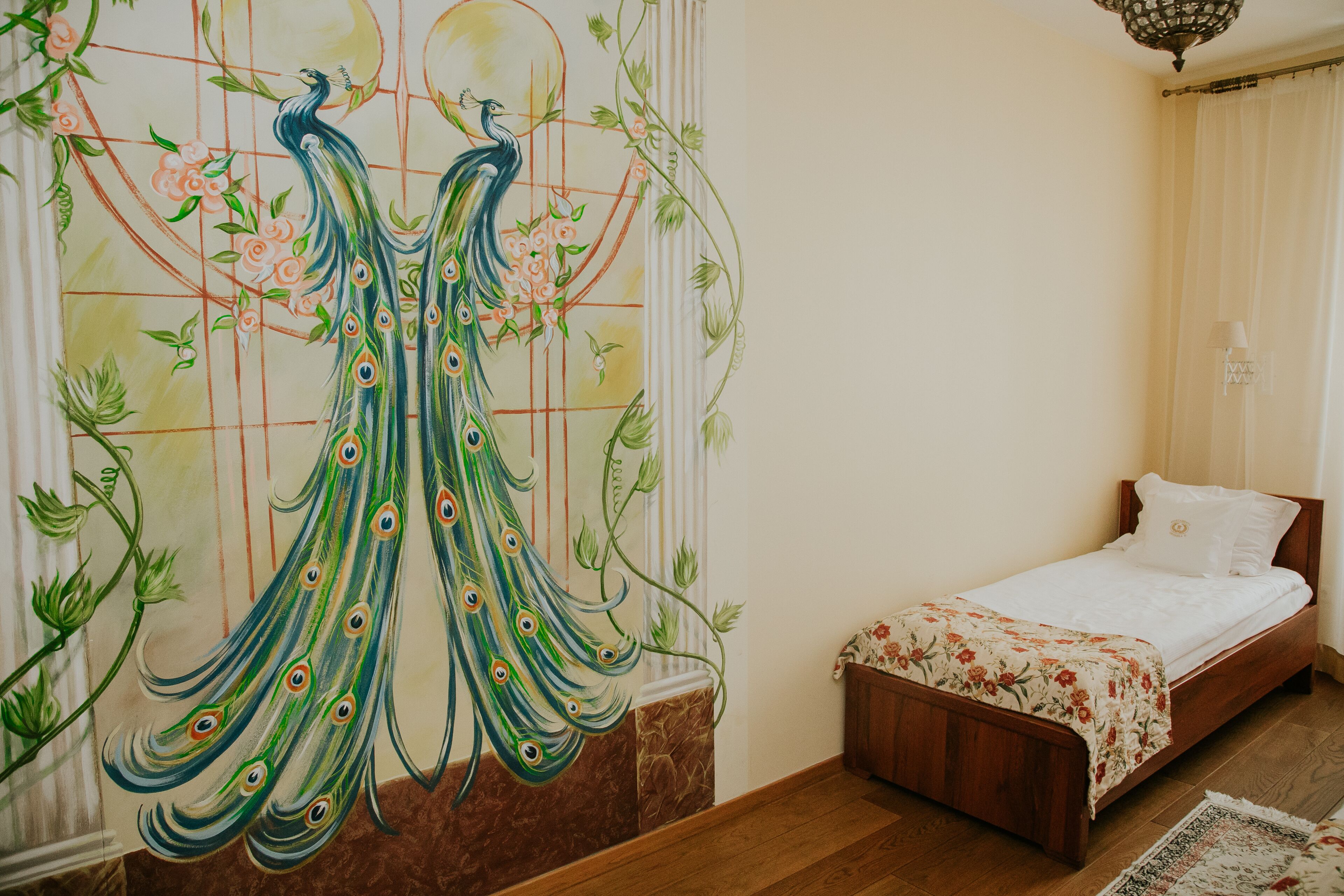 Une chambre à coucher avec un lit, une couvre-lit à motifs floraux et une fresque représentant un paon sur le mur.
