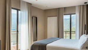 Un dormitorio moderno con una cama grande, una mesita auxiliar y vistas a un paisaje montañoso a través de las ventanas.