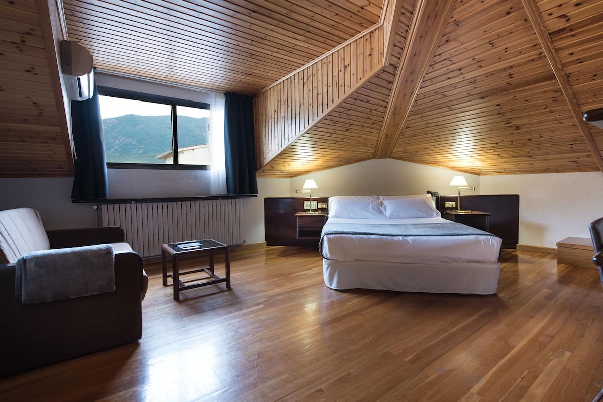 A bedroom with a wooden ceiling, a bed, a nightstand, a lamp, a window with a view, and a chair.
