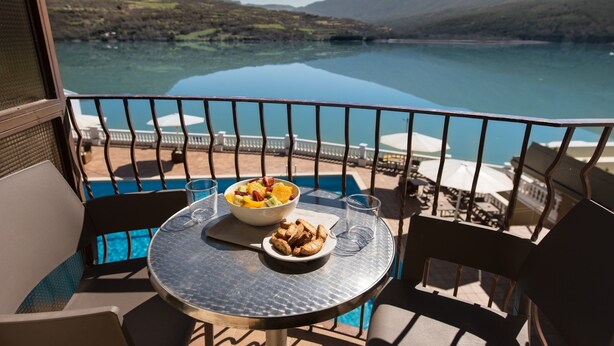 Un balcón con una mesa lista para el desayuno, con vistas a un lago y montañas.