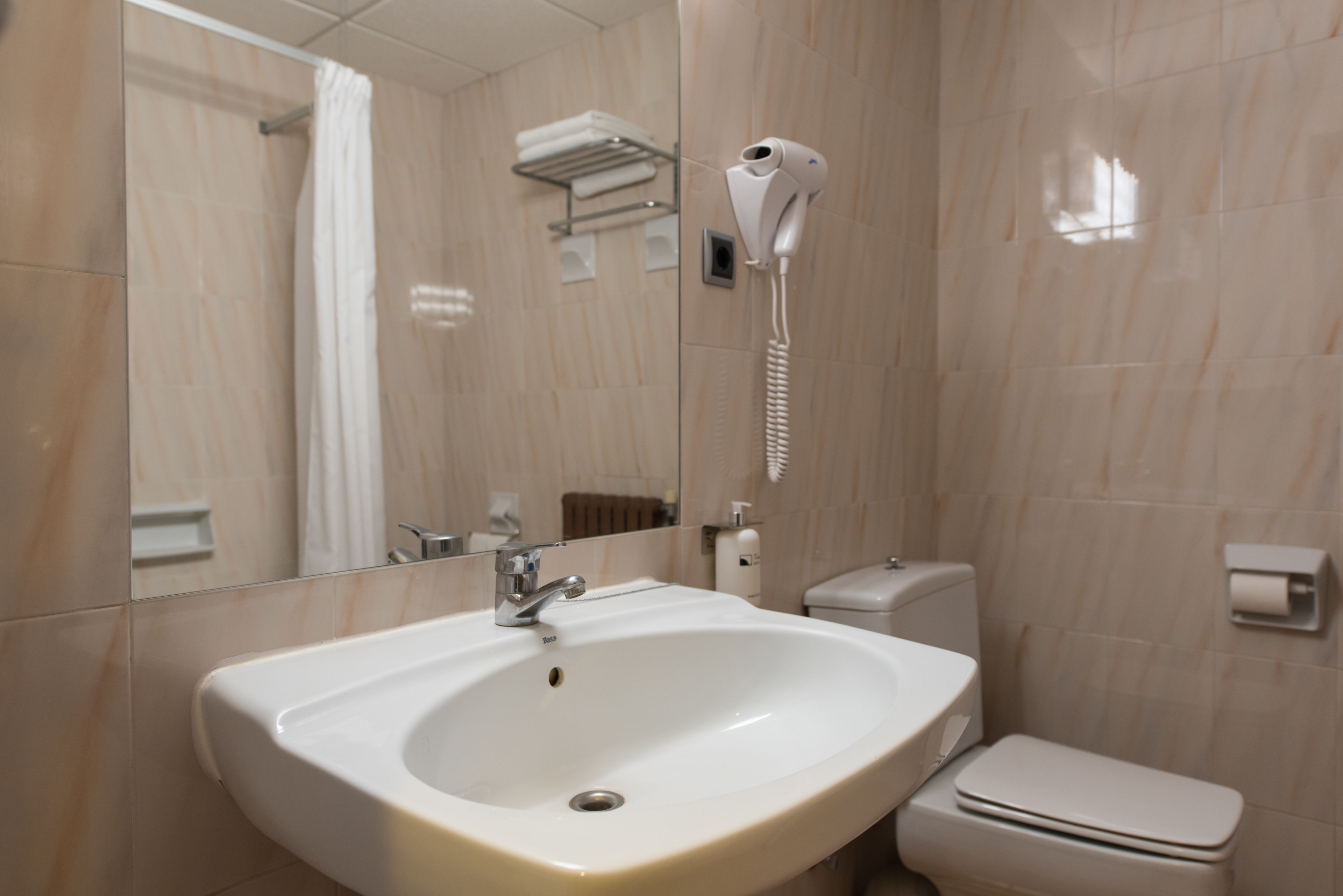 A bathroom with a sink, toilet, and a hairdryer mounted on the wall.