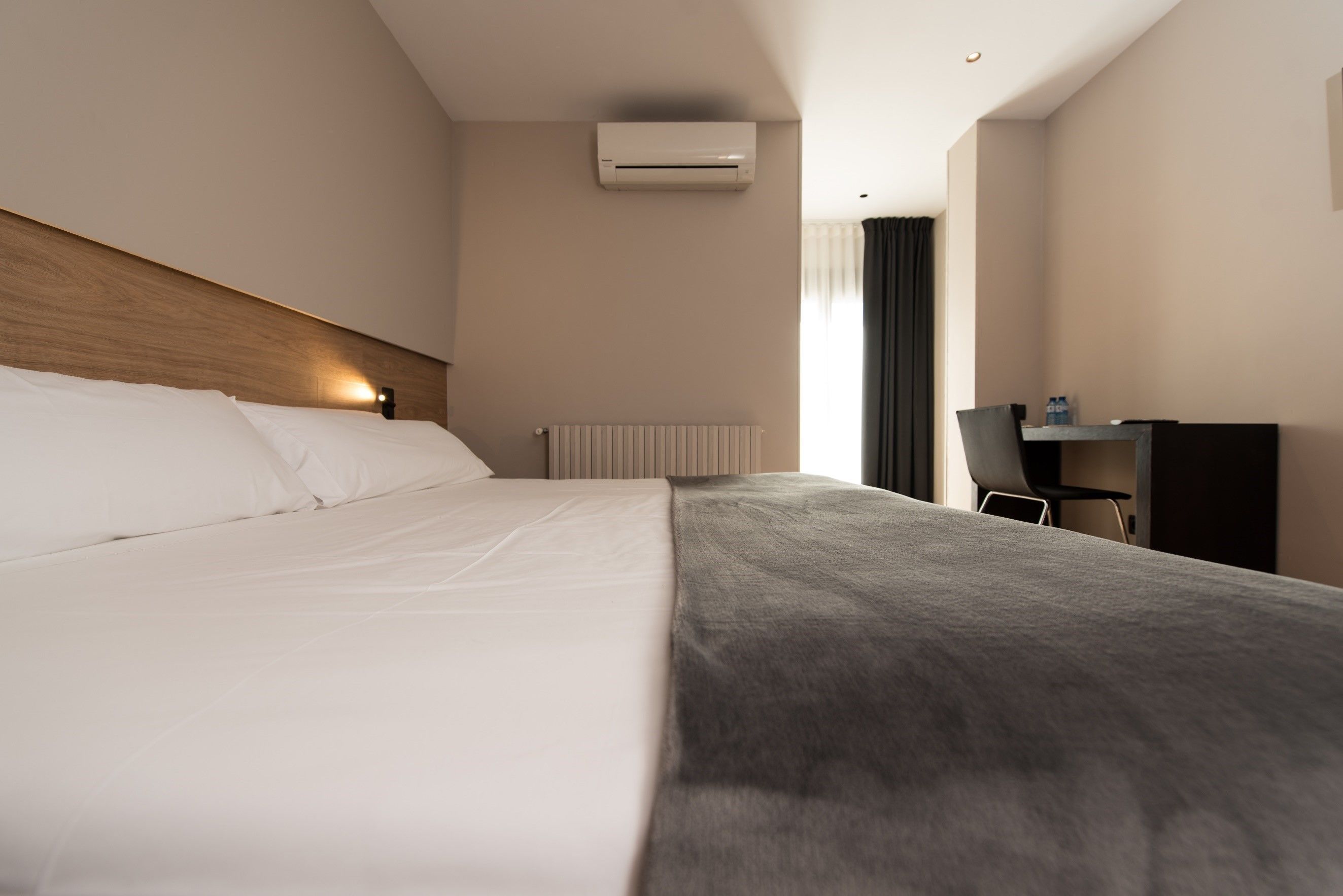 A modern hotel room with a large bed, a desk, and an air conditioning unit.