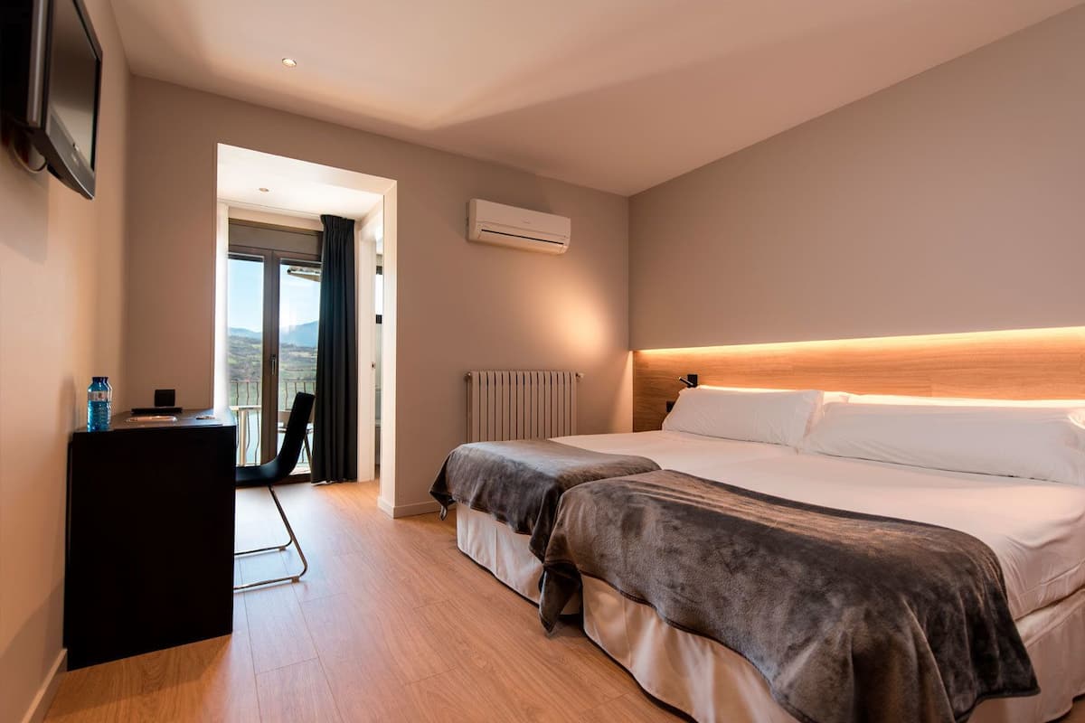 A modern hotel room with a large bed, a bedside table, a radiator, and a view of the outdoors.