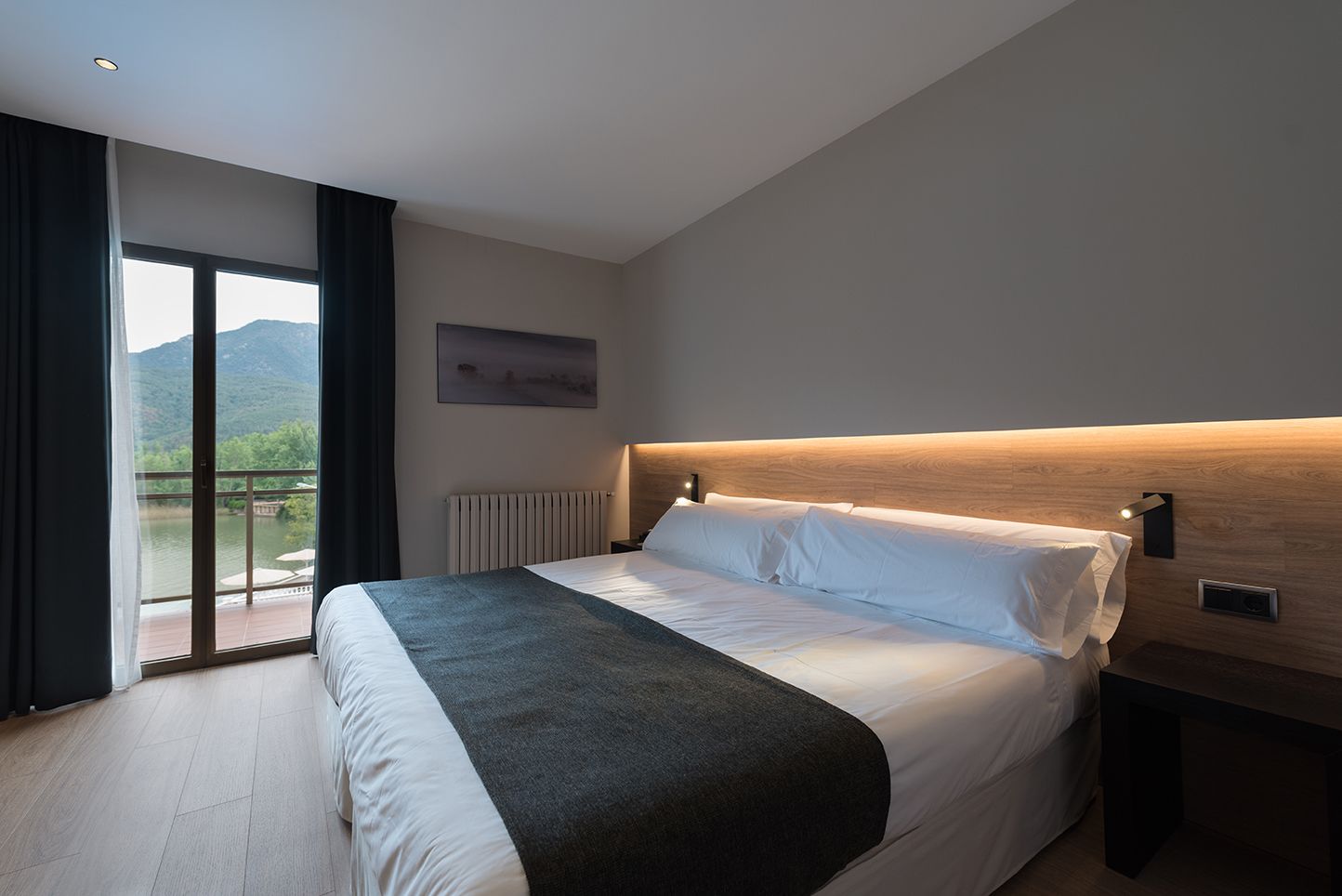 Ein modernes Hotelzimmer mit einem großen Bett, Bergblick durch eine Schiebetür und einem Holzkopfende.