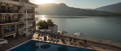 A hotel with a swimming pool, outdoor seating, and a view of a lake and mountains.