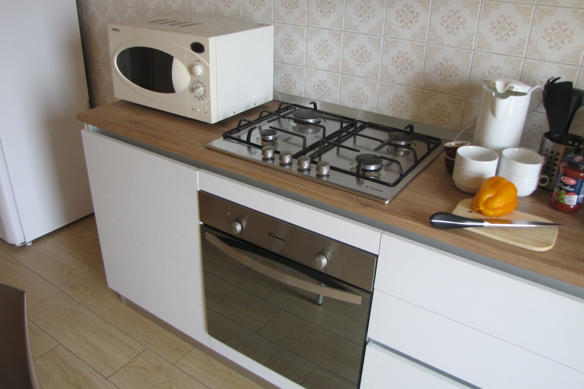 Een keuken met een fornuis, oven, magnetron en diverse keukengerei.