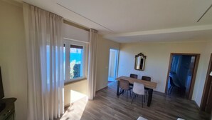 Amplia sala de estar con mesa de comedor, sillas, sofá y vista al mar a través de una ventana.