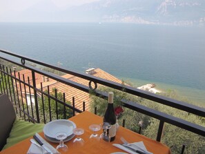 Una mesa con una botella de vino, copas y cubiertos, con vistas a la costa y montañas al fondo.