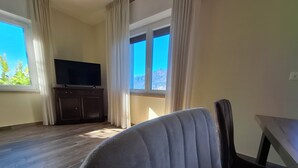 Una habitación con piso de madera, un televisor sobre un mueble y una silla.
