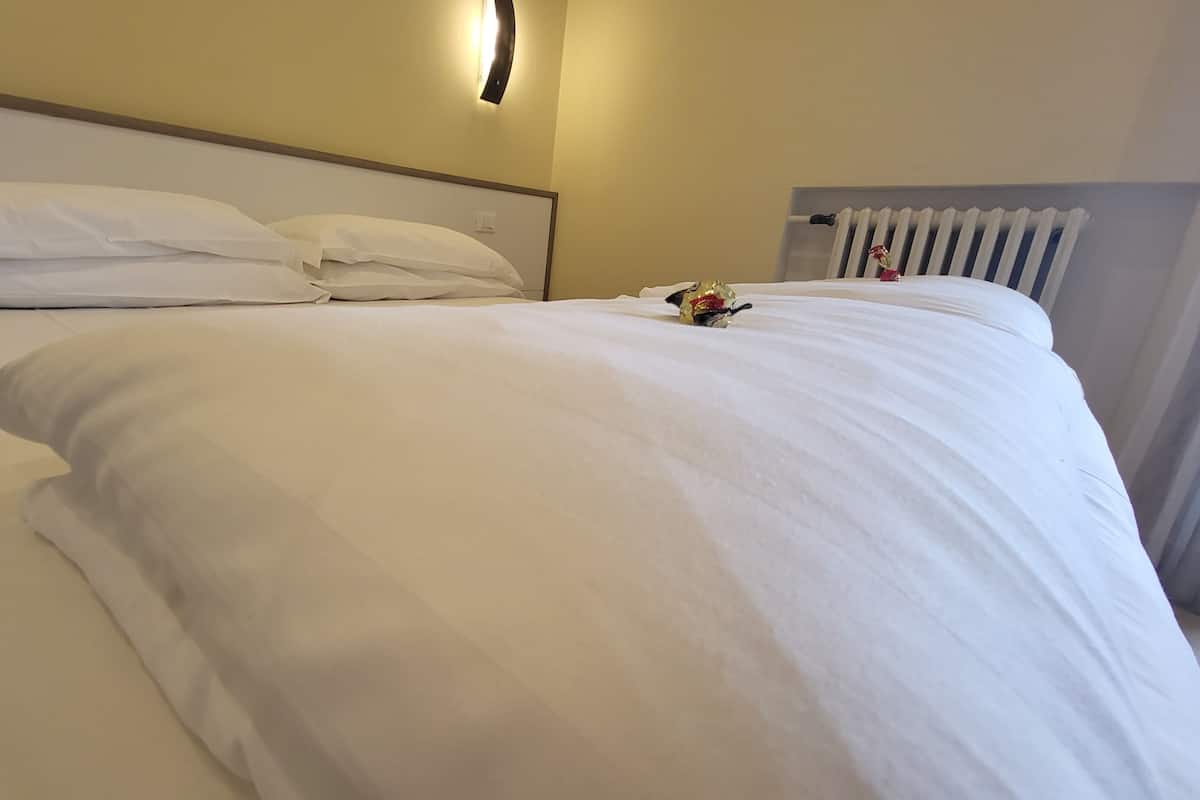 Een net opgemaakt bed met witte lakens, een hoofdbord en een wandlamp.