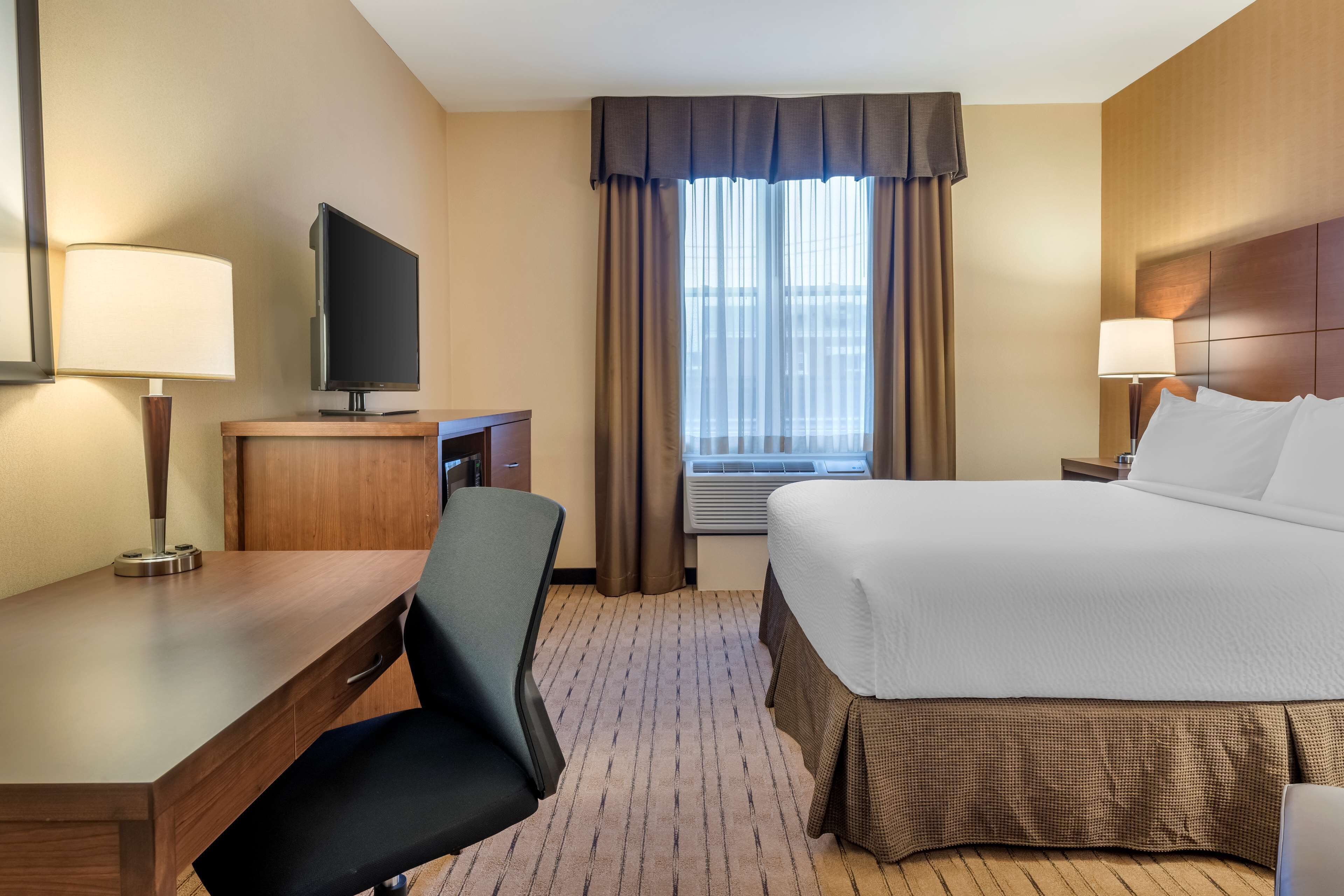 A hotel room with a bed, desk, chair, TV, and window with curtains.