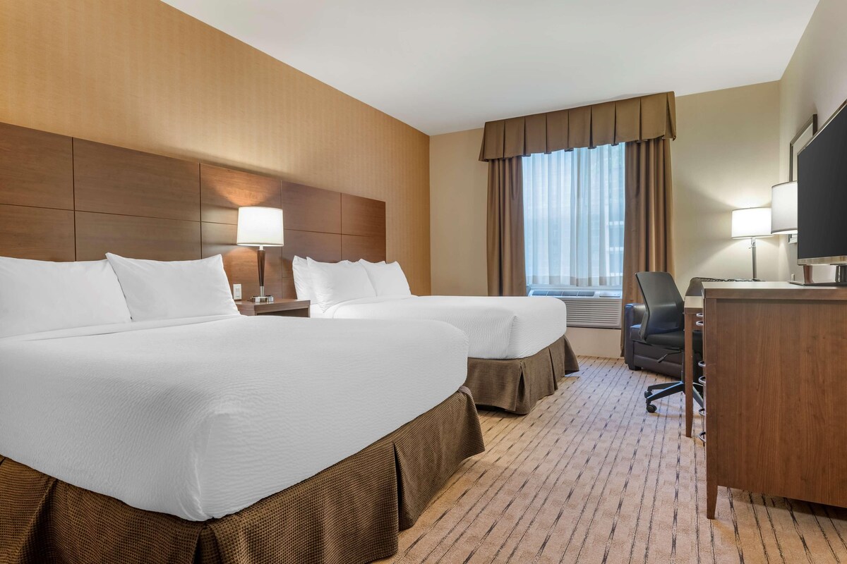 A hotel room with two beds, a desk, a chair, and a TV.