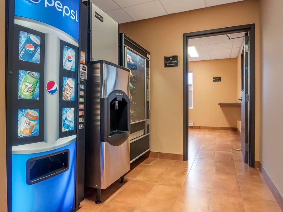 Ein Flur mit einem Getränkeautomaten, der Pepsi und 7UP anbietet, einem Wassenspender und einem Schild, das einen Gemeinschaftswaschraum kennzeichnet.