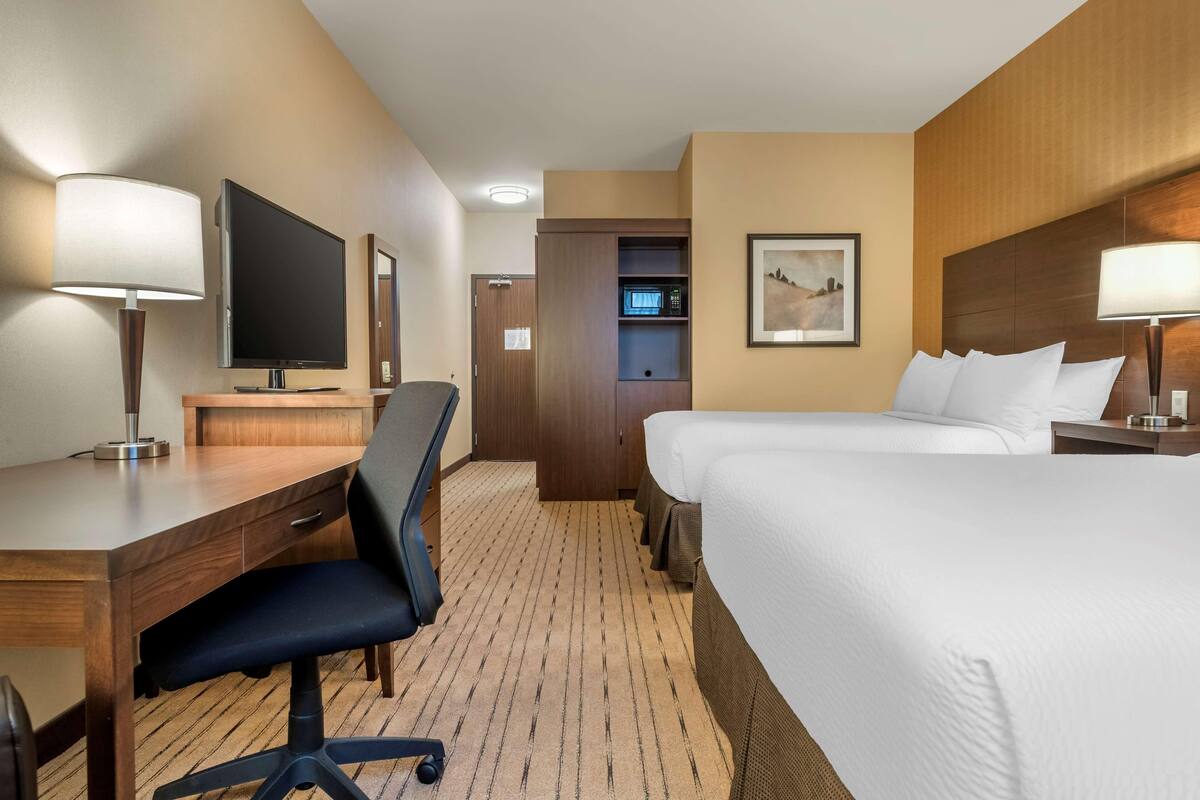 A hotel room with a desk, chair, TV, two beds, and a microwave.