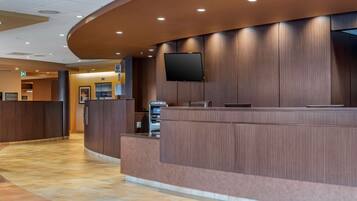 A reception area with a curved counter, a flat-screen TV mounted on the wall, and an ATM machine.