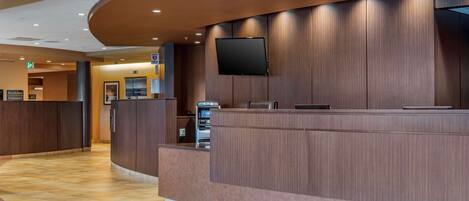 A reception area with a curved counter, a flat-screen TV mounted on the wall, and an ATM machine.