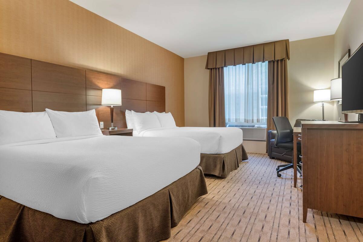 A hotel room with two beds, a desk, a chair, and a TV.