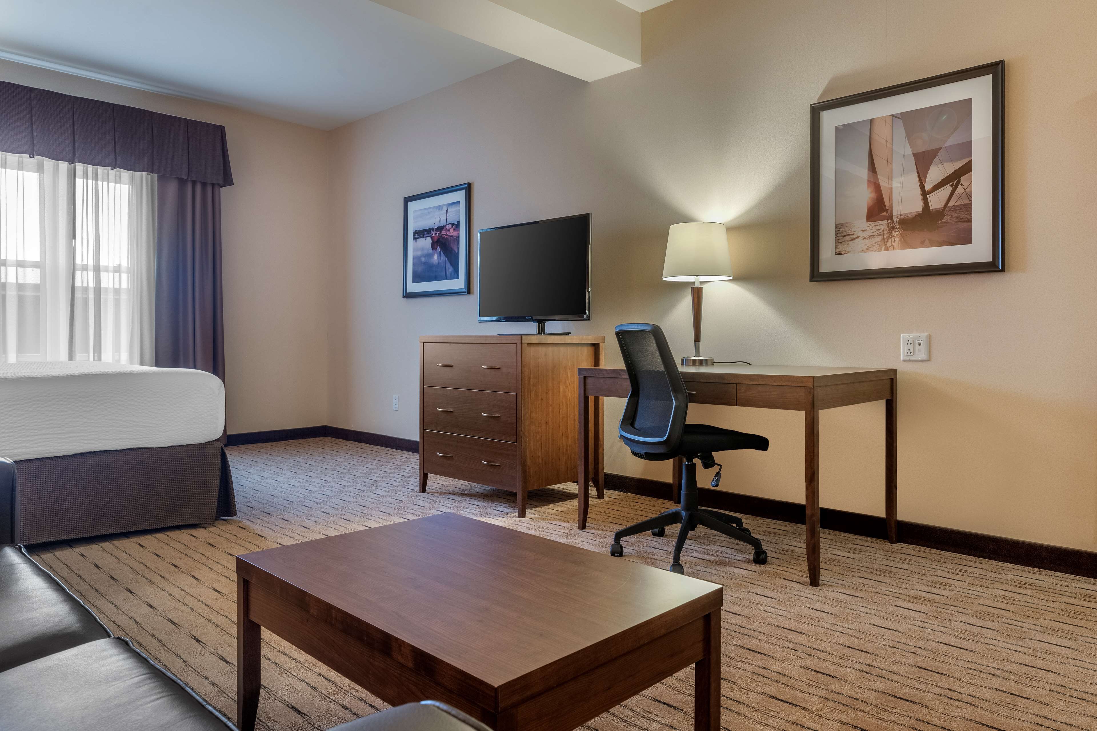 A hotel room with a bed, a desk with a chair, a television, a lamp, and a framed picture on the wall.