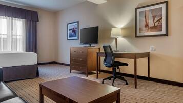 A hotel room with a bed, a desk with a chair, a television, a lamp, and a framed picture on the wall.