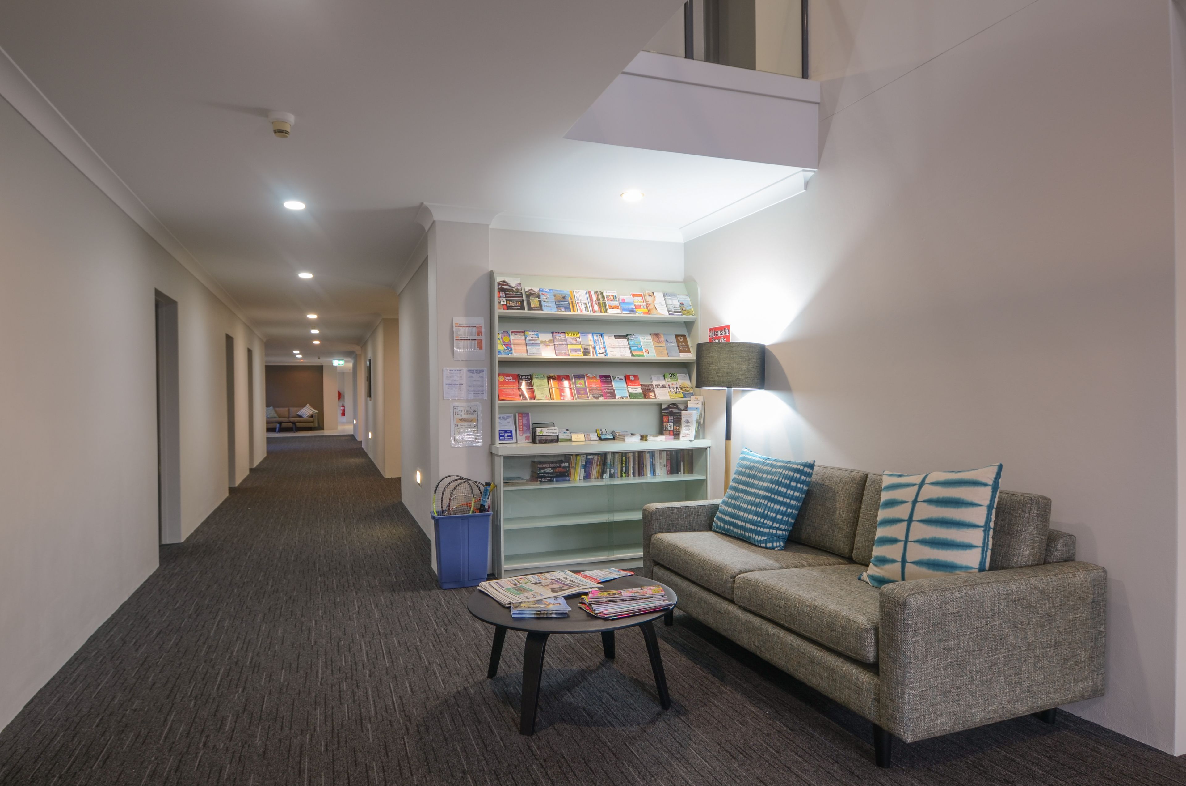 A hallway with a sofa, a small table with magazines, and a bookshelf filled with books.
