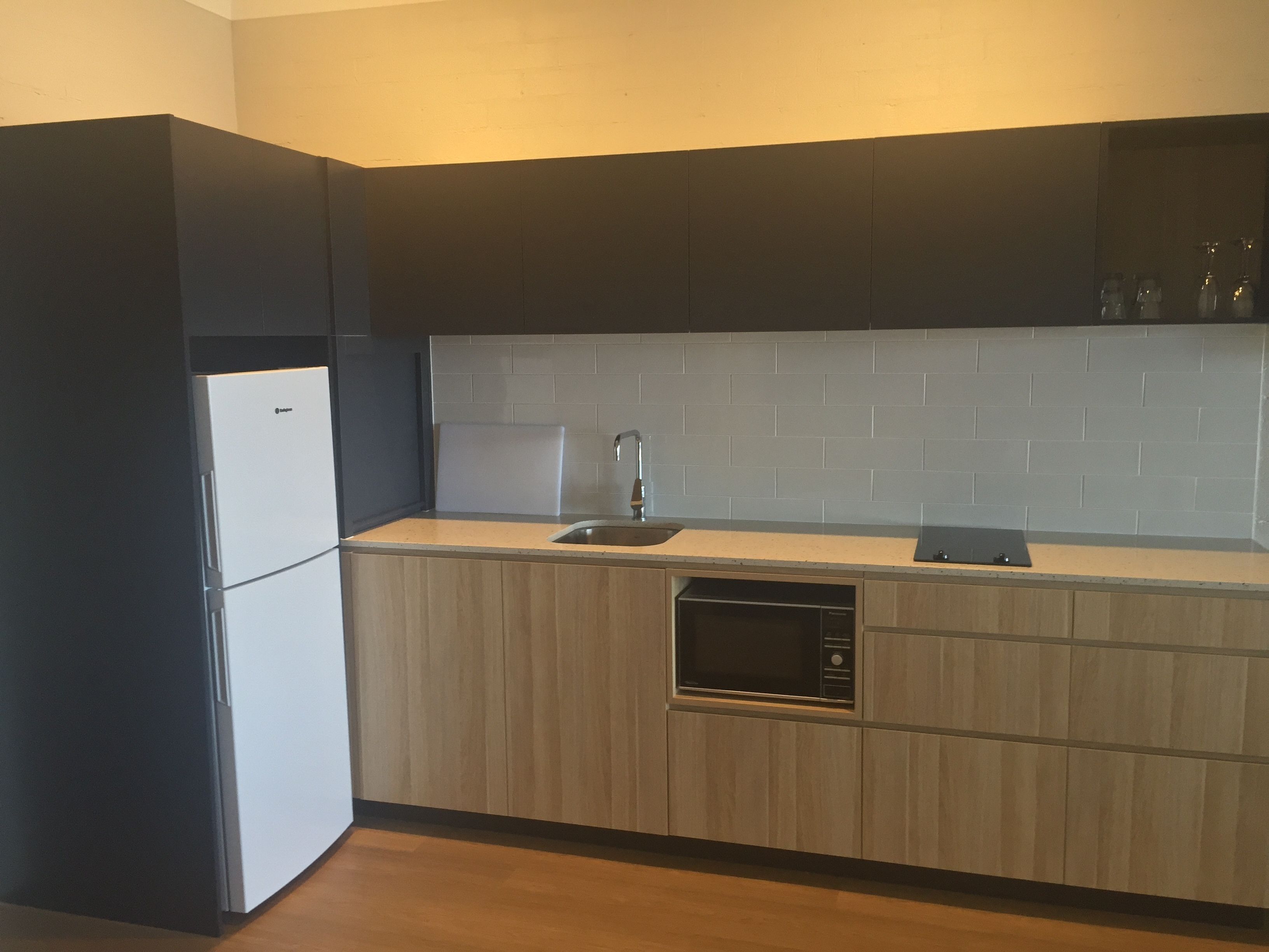 Una cocina compacta con refrigerador integrado, microondas y pileta.