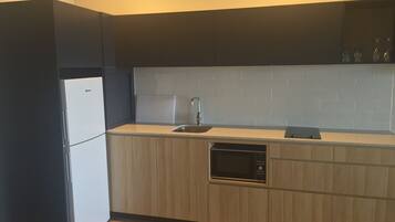 Una cocina compacta con refrigerador integrado, microondas y pileta.