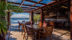 An outdoor dining area with wooden tables and chairs, overlooking a body of water. - Moby Dick Waterfront Resort Motel (Yamba)