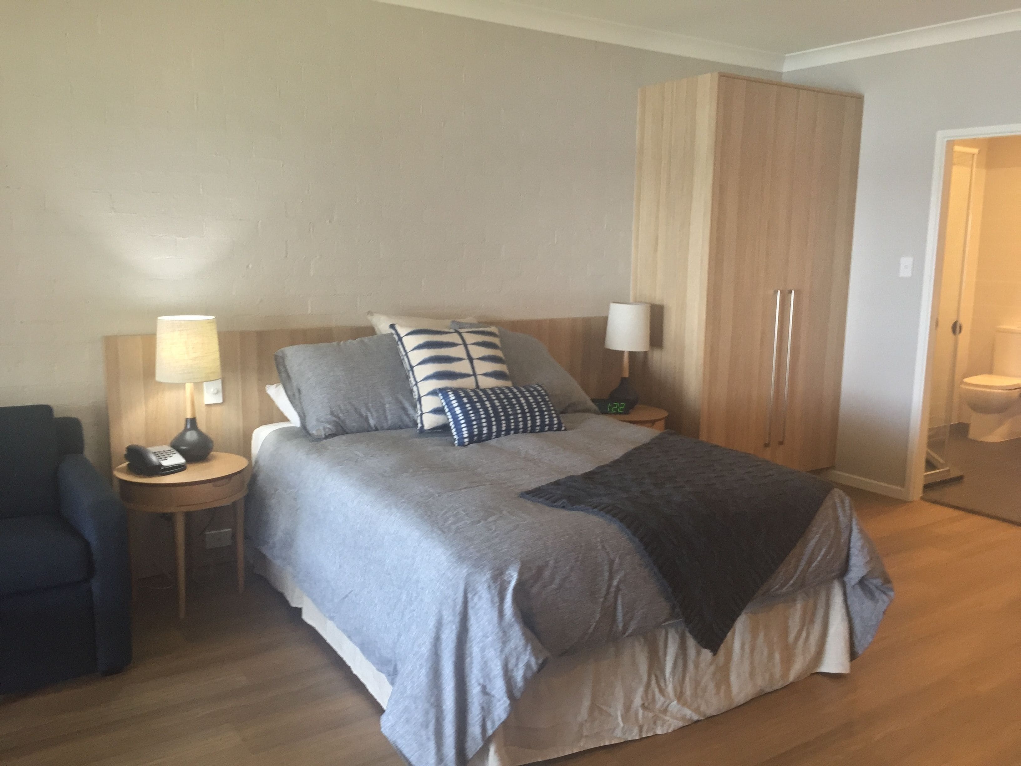 A hotel room with a bed, two bedside tables, a chair, a wardrobe, and a bathroom.