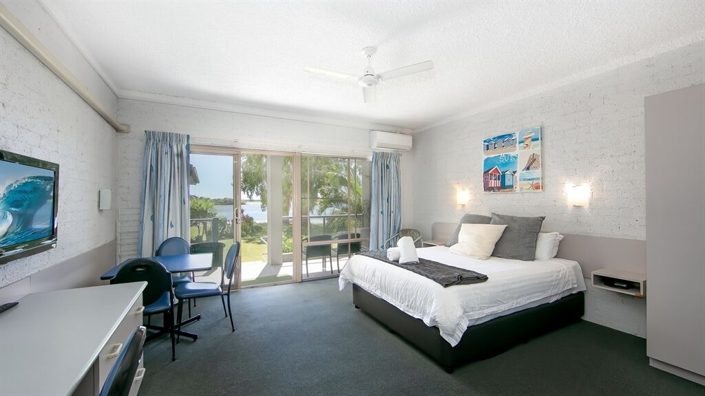A hotel room with a bed, desk, and chair, a balcony with a view, and a ceiling fan.