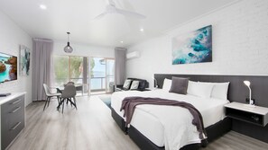 Un dormitorio moderno con una cama grande, un escritorio y una silla. Hay un cuadro en la pared y vistas al exterior por la ventana.