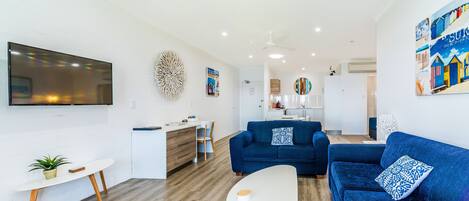 A modern living room with a blue sofa, a white coffee table, and a flat-screen TV mounted on the wall.