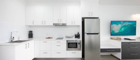 Een moderne keuken met witte kastjes, een roestvrijstalen koelkast, een magnetron en een flatscreen televisie.