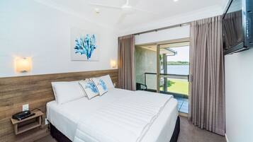 Quarto de hotel com cama, mesa de cabeceira, televisão na parede, ventoinha no teto e janela com cortinas.