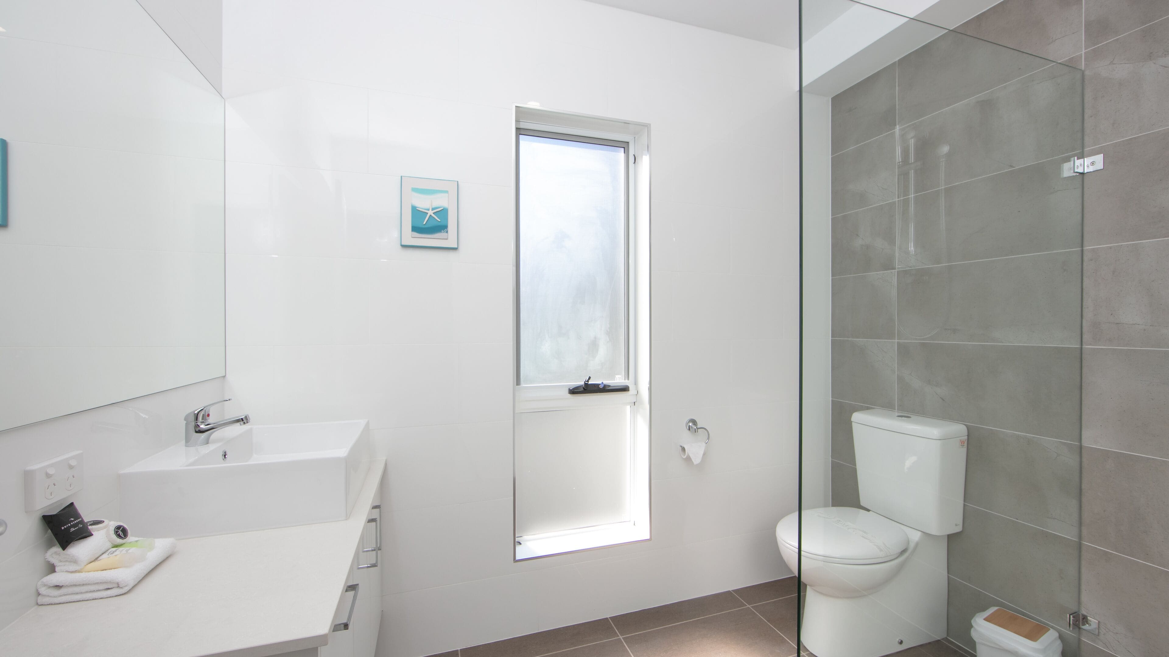 A modern bathroom with a white sink, a mirror, a toilet, and a shower area.