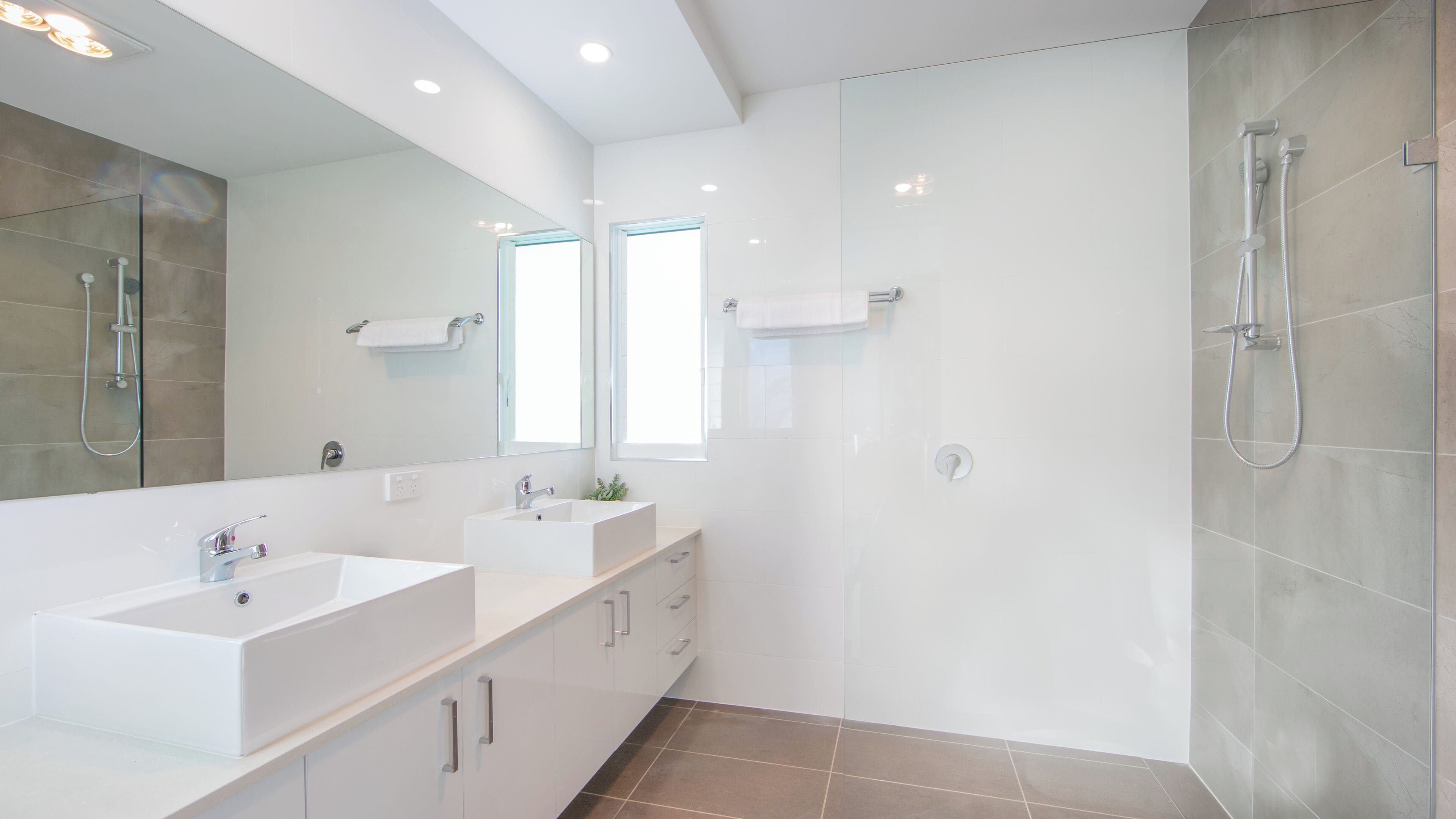 A modern bathroom with two sinks, a large mirror, and a glass-enclosed shower.