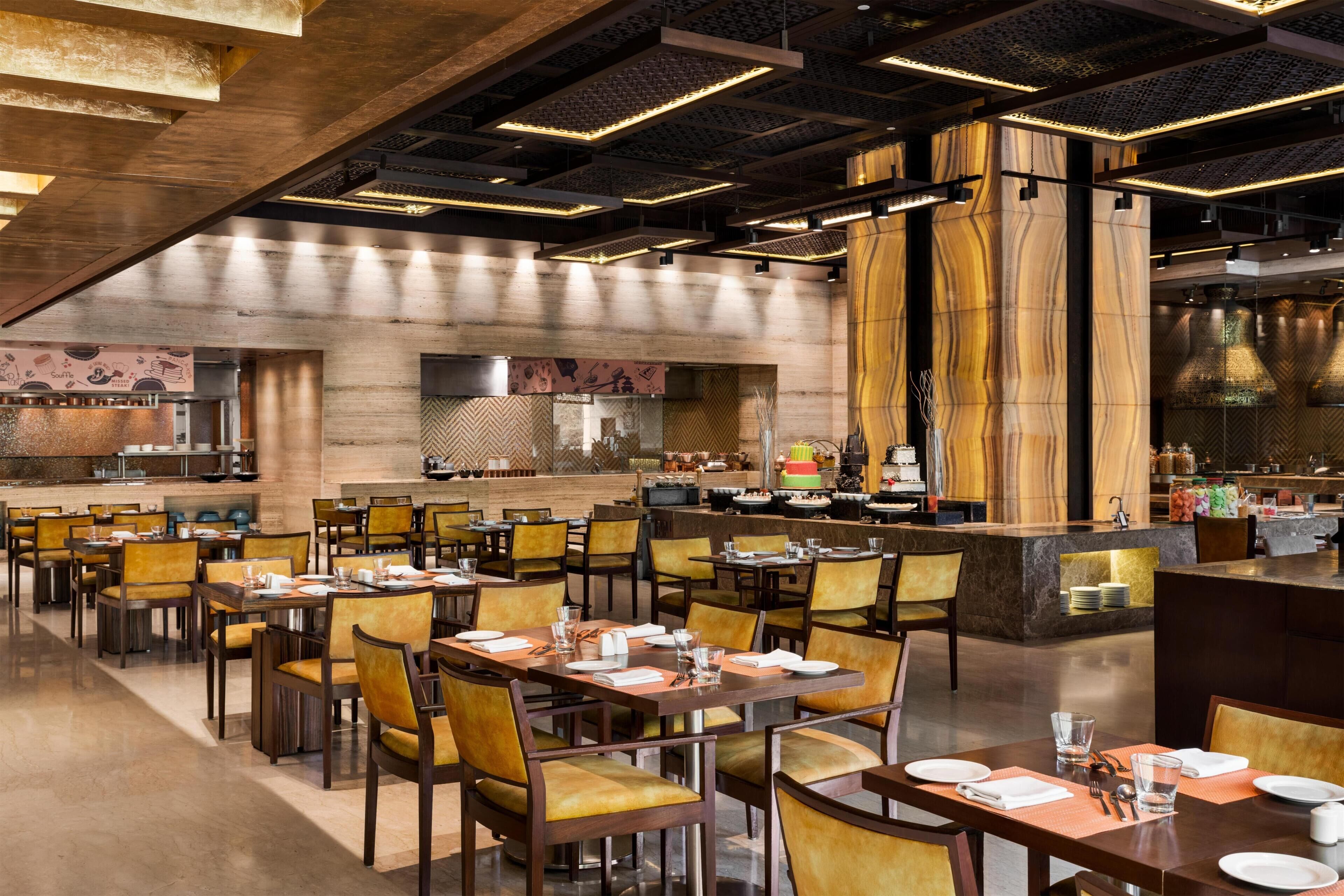 A spacious dining area with multiple tables and chairs, a central bar, and a kitchen in the background.