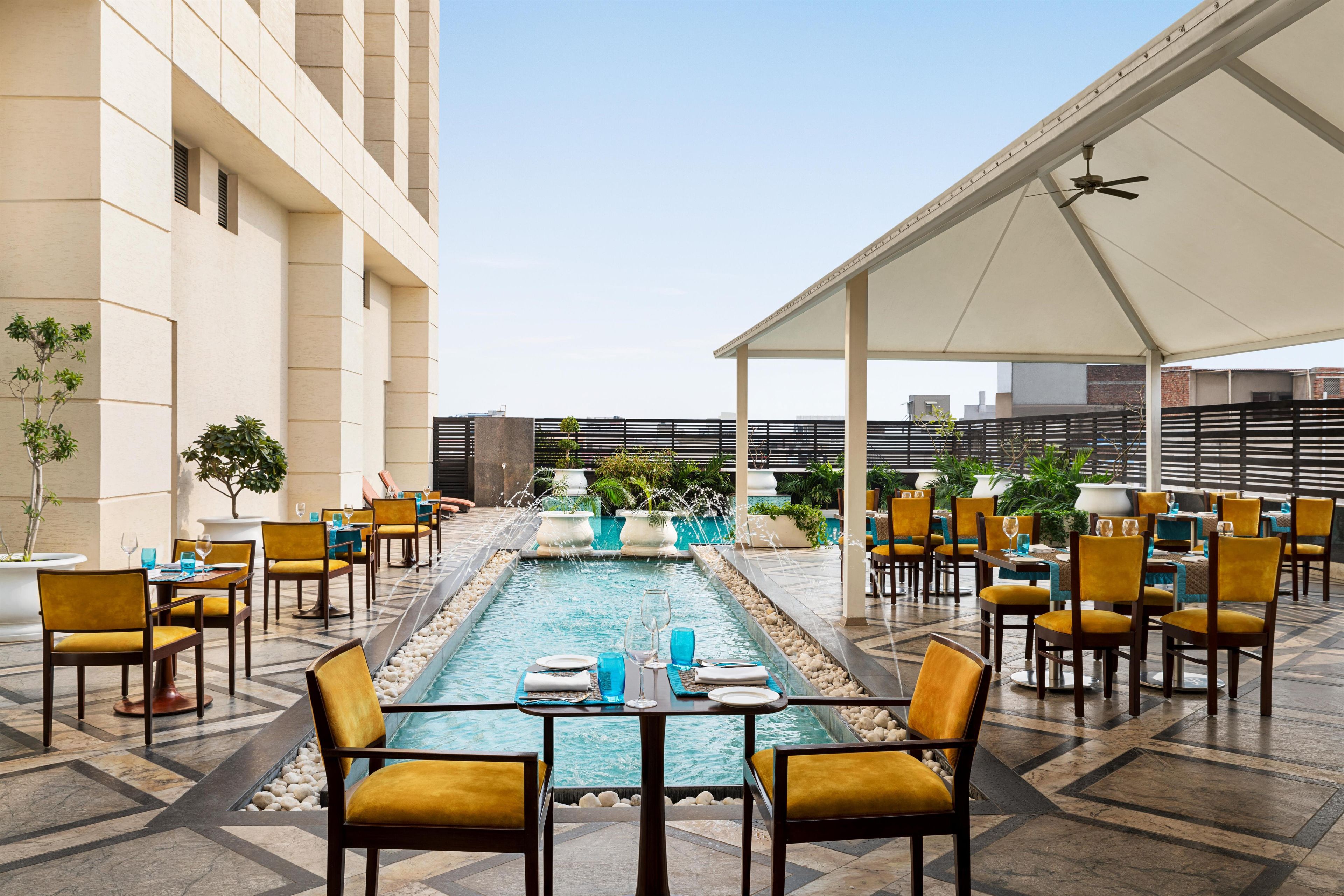 A rooftop dining area with tables and chairs, a pool, and a covered seating area.